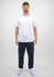 A man stands wearing a white t-shirt and navy blue track pants. The pants have a logo on them.