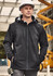 A man wearing a black unisex softshell jacket with a hood, standing at a construction site. He has a hard hat on.