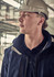 A person wearing a hard hat and a navy blue softshell jacket, looking thoughtfully into the distance.