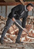A man wears a black full zip sherpa fleece jumper with grey accents, standing in front of stacked logs.