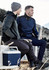 A grey and navy unisex hoodie is worn by two men sitting outdoors, one holding a drink bottle and a cooler nearby.