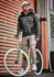 A man wearing a grey reinforced knit hoodie sits on a green bicycle against an orange corrugated backdrop.