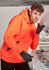 An orange unisex water-resistant hoodie with a black logo, worn by a person in a workshop setting.
