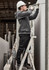 A person in a grey zip front multi-pocket hoodie and black pants using a drill while standing on a ladder.