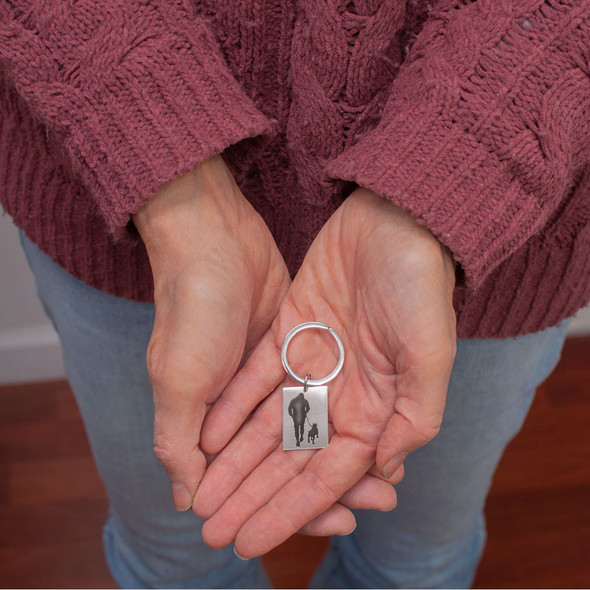 Model holding silver keyring with rectangle charm, engraved with silhouette of a man walking his dog