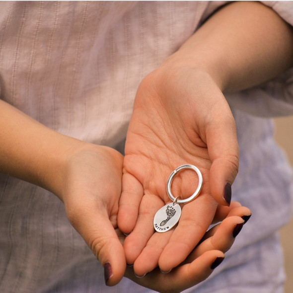 model holding custom sterling silver oval footprint keychain with your child's actual footprint, personalized with hand stamped name