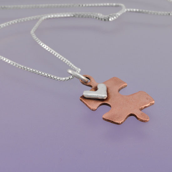 Handmade copper puzzle piece charm with silver heart on a necklace, shown from the side