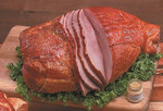 Hickory Smoked Sugar Cured Ham (Spiral Whole), sliced ham showing a spiral cut, smoked sugar-cured ham on a wooden cutting board with greens and a small jar of mustard.