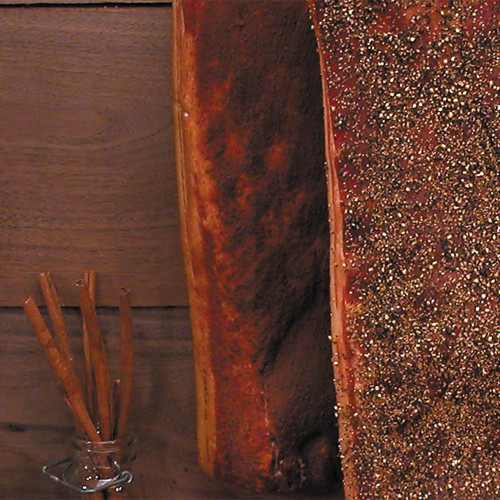 Sugar Cured Hickory Smoked Cinnamon Bacon - 1lb Package, close-up of smoked bacon with a crispy, glossy surface and sprinkles of cinnamon, on a wooden surface with cinnamon sticks in a glass jar.