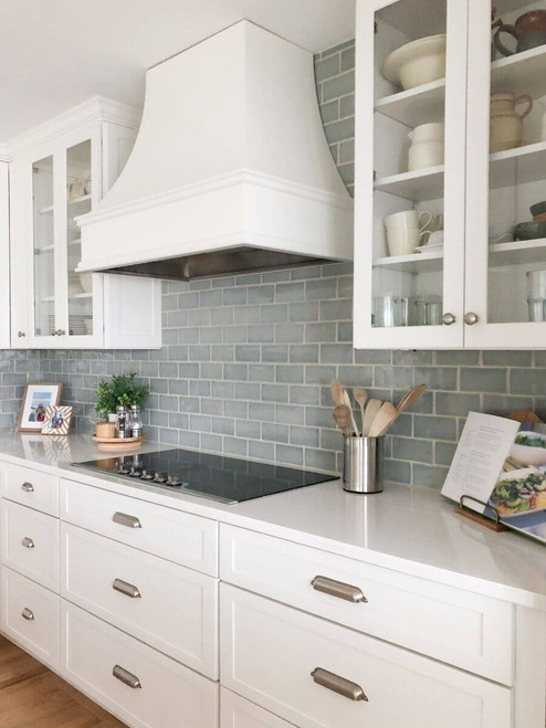 Classic blue and white kitchen with white range hood, blue tile backsplash, and glass-front cabinets