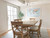 Warm wood dining table with upholstered chairs and light blue area rug under a classic chandelier in a bright dining room