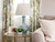 Blue ceramic gourd table lamp on a round gold side table against patterned grandmillennial curtains