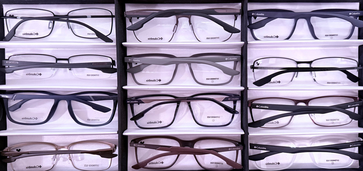 Twelve Columbia optical frames from Kit #8 displayed in a tray, featuring sporty rectangular silhouettes in matte navy, satin black, brown horn and crystal grey finishes with extended 150 mm temples.