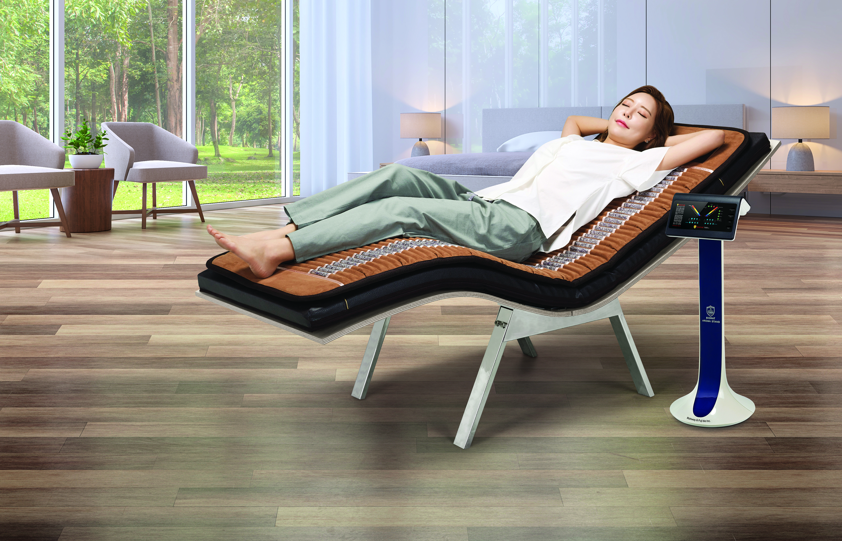 Woman laying on a Professional Amethyst Biomat on top of a BioAcoustic Mat with an Aroma Stand next to her in a big room with wood floors, sheer white drapes, two chairs and two lamps