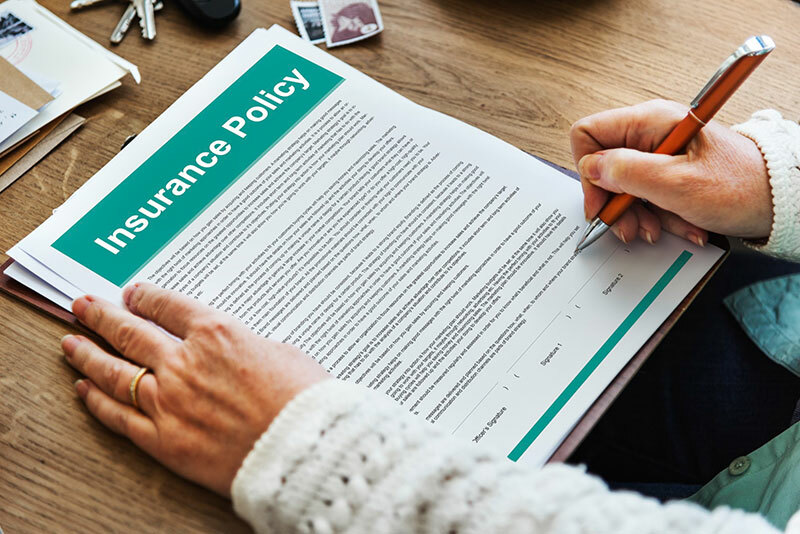 Insurance policy on a desk with someone signing it. 