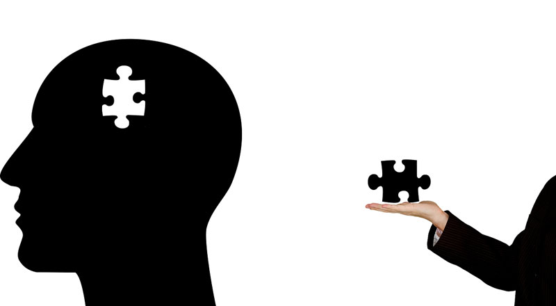 Illustration of the profile view of a human head with a puzzle piece missing from it with a arm and hand outreached behind it with the missing piece to indicate help for mental health