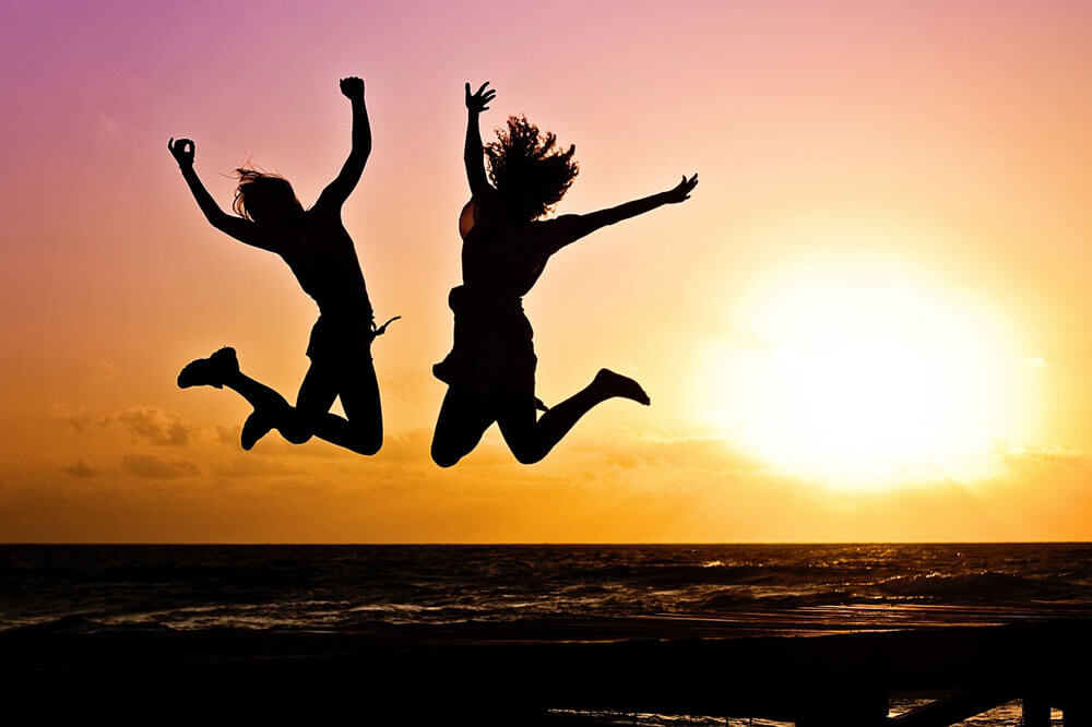 Two people jumping on the beach against a sunset