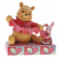 Disney Traditions Piglet and Winnie the Pooh sit close beside each other as they trace and snip a handmade garland of hearts figurine