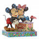 Disney Traditions Minnie leans over a kissing booth to plant a smooch on one very smitten Mickey Mouse figurine