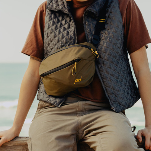 Peak Design Outdoor Sling 7L (Kelp) - Sitting by the ocean wearing the Outdoor Sling 7L Kelp