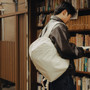 A person in a dark brown leather jacket and black pants moon color backpack while browsing bookshelves. | Peak Design official