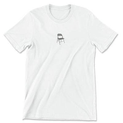 White unisex tee with an imprint of a folding chair on the front, and a quote from Shirley Chisholm on the back that reads If they don’t give you a seat at the table, bring a folding chair