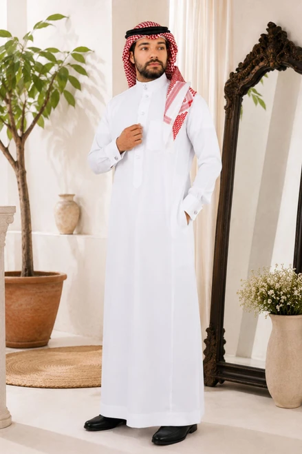 Man in traditional white thobe with red scarf standing in a room with decorative elements.