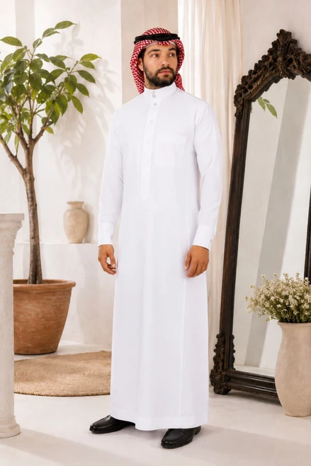 Man in a white thobe standing in a room with decorative elements.