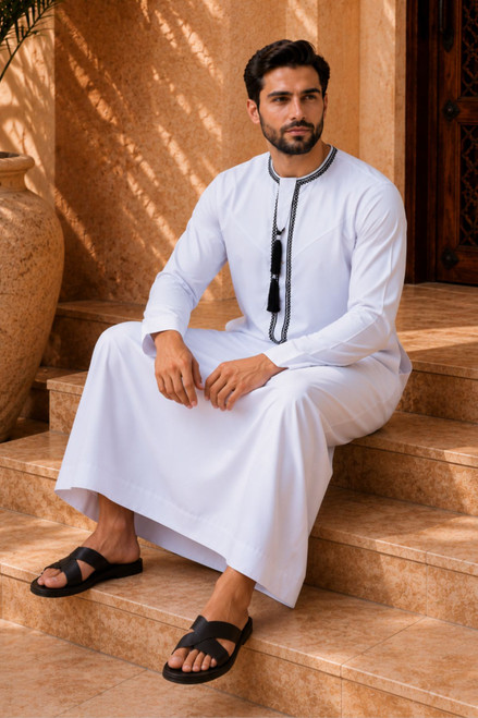 Man in traditional white middle eastern clothing with black details sitting on steps.