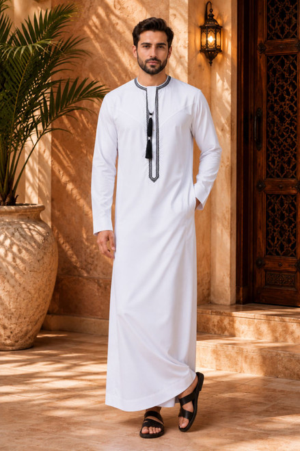 Man wearing a traditional white thobe with black details in an outdoor setting.