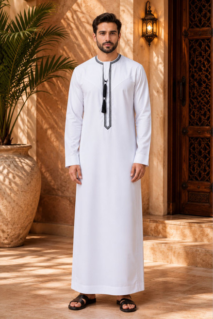 Man wearing a traditional white thobe with black details in an outdoor setting.