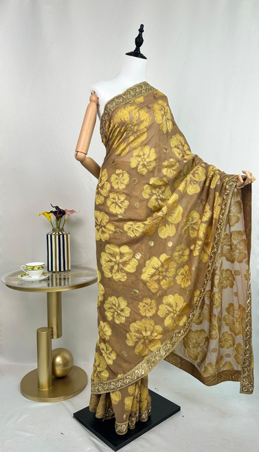 Luxurious Taupe Organza Saree with Golden Floral Motifs & Embroidered Border Luxurious Taupe Organza Saree with Golden Floral Motifs & Embroidered Border