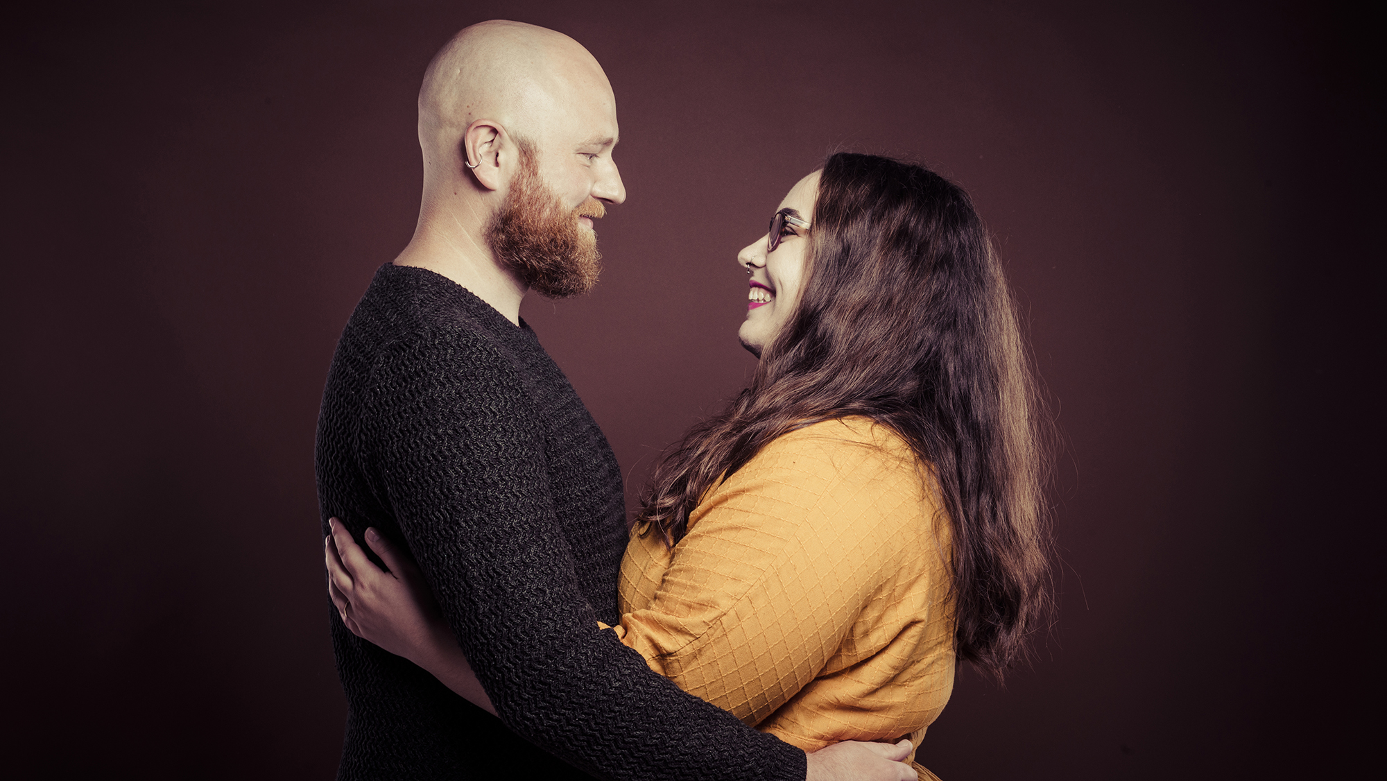 couple embracing each other on a dark studio background during a couples photo shoot with Emotion Studios