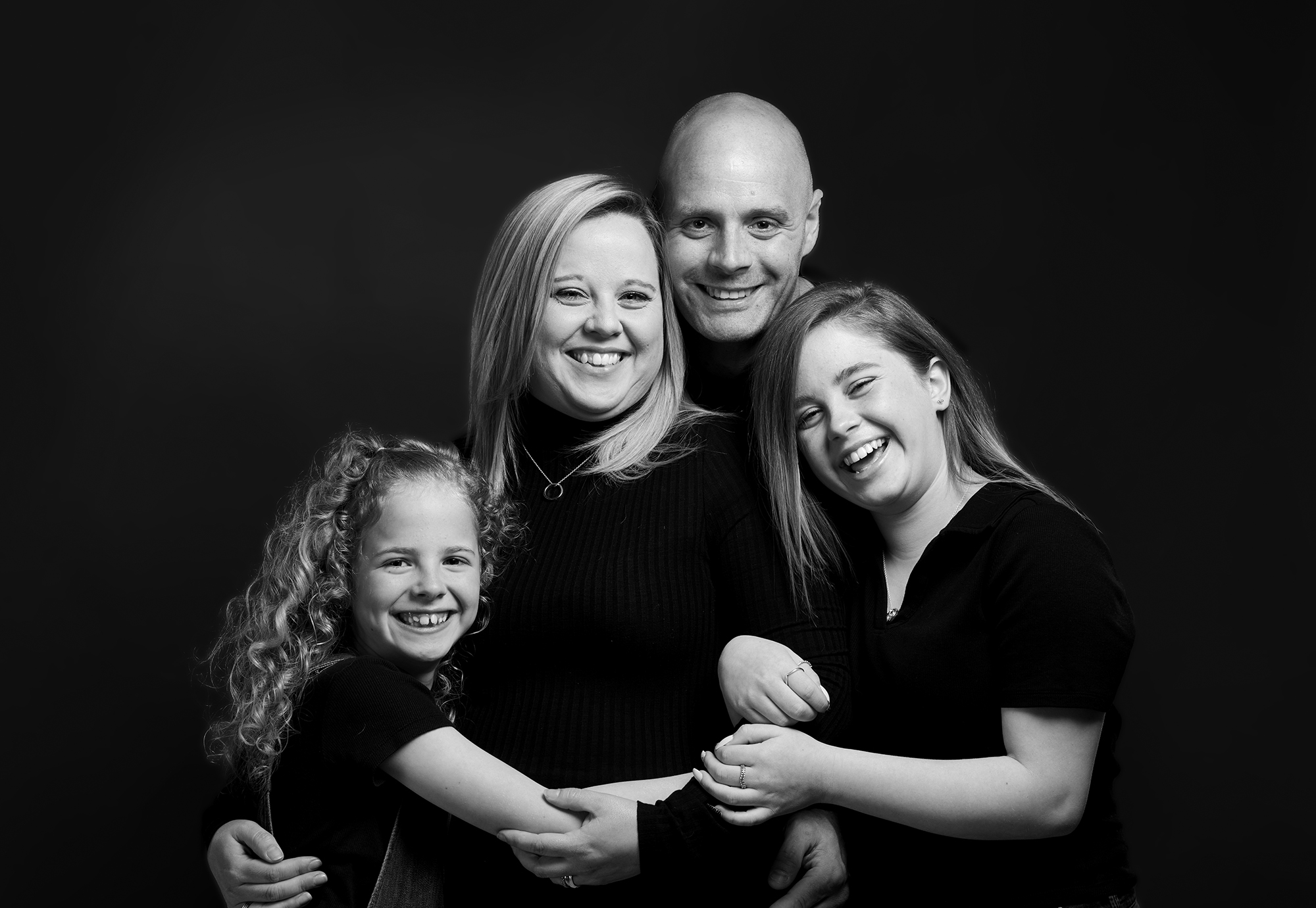 b&w family photograph on black background showing a family of four photographed by Emotion Studios