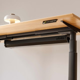 Système de gestion des câbles ofinto noir, fermé, sur le bureau réglable en hauteur Elevate – gros plan de la goulotte noire sous un plateau en bois certifié FSC