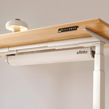 Système de gestion des câbles ofinto blanc, fermé, sur le bureau réglable en hauteur Elevate – gros plan de la goulotte blanche sous un plateau en bois certifié FSC