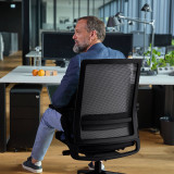 Un homme est assis de manière saine et confortable au bureau sur une chaise de bureau ergonomique Active coloris noir mat