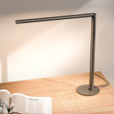 Lampe de bureau ofinto Lumino Desk graphite avec base – lampe LED sur un bureau en bois avec un magazine ouvert ; éclairage de poste de travail moderne et minimaliste