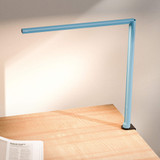 Lampe de bureau ofinto Lumino Desk bleue avec pince de table noire (en option) – lampe LED sur un bureau en bois avec un magazine ouvert ; éclairage de poste de travail moderne et minimaliste