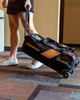 900 Global 3‑Ball Travel Tote Pro Black Gold rolling on a bowling center concourse with balls visible through the clear top