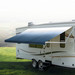 Slate blue awning extended out on an RV in a clearing.