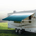 Blue awning extended out on an RV in a clearing.