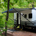 Black manual RV awning assembly open on an RV in the woods.