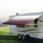 Burgundy awning extended out on an RV in a clearing.