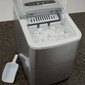 RV portable ice maker with the ice box door open and it is filled with ice. It sits on the counter with the ice scoop.