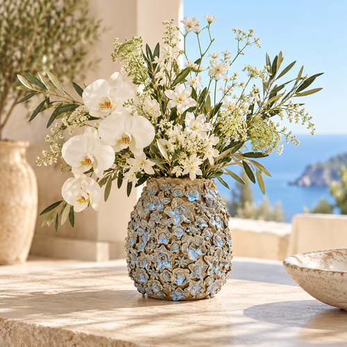 Earth tone and blue Bouquet De Fleurs ceramic vase styled with white flowers in a sunlit coastal setting.