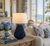 Handmade Thai blue anemone ceramic table lamp on an end table beside a sofa in a bright coastal living room.