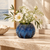 Ocean blue sea urchin ceramic vase with delicate white flowers on a warm stone console