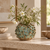 Handmade Thai moss green ceramic vase with delicate flowers in a warm neutral interior