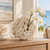 Ivory coral ceramic vase with delicate white orchids displayed on a natural wood console in an elegant coastal interior.